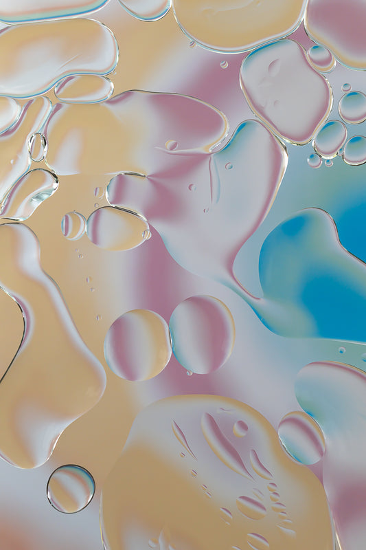 "Rainbow Splatter" is an abstract acrylic photo print featuring a macro photograph of oil and water. The image displays a vivid mix of colors including orange, pink, white, green, and blue, creating a pattern that resembles a splatter painting. This contemporary art piece, part of the Rainbow Rhapsody collection, can be displayed alone or with other similar artworks. It evokes a sense of dynamic movement and vibrant energy.