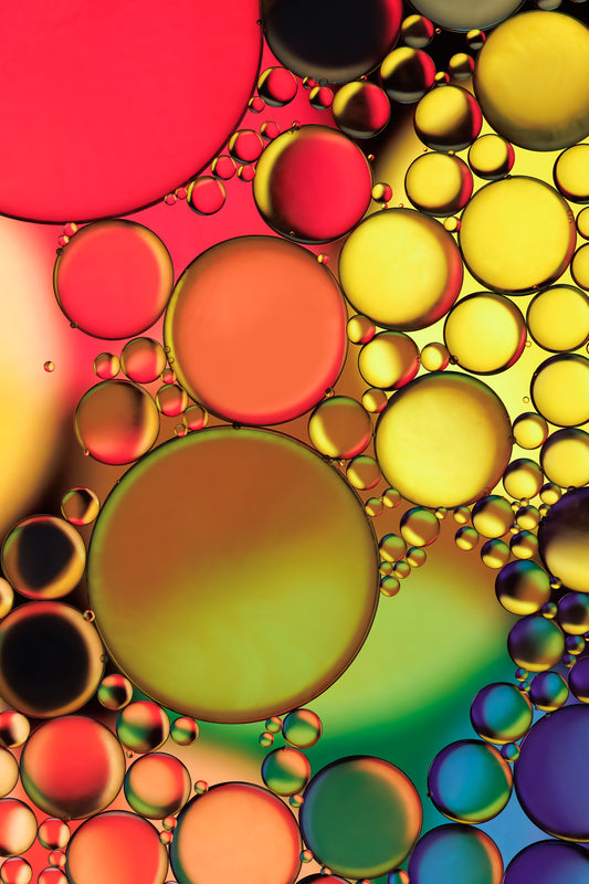 Abstract photograph titled "Jewels" featuring an interplay of oil and water in vibrant orange, yellow, green, blue, and purple hues, printed on high-grade photo paper and mounted under acrylic for depth and clarity. The predominant elements of this image are circular forms and vibrant hues. 
