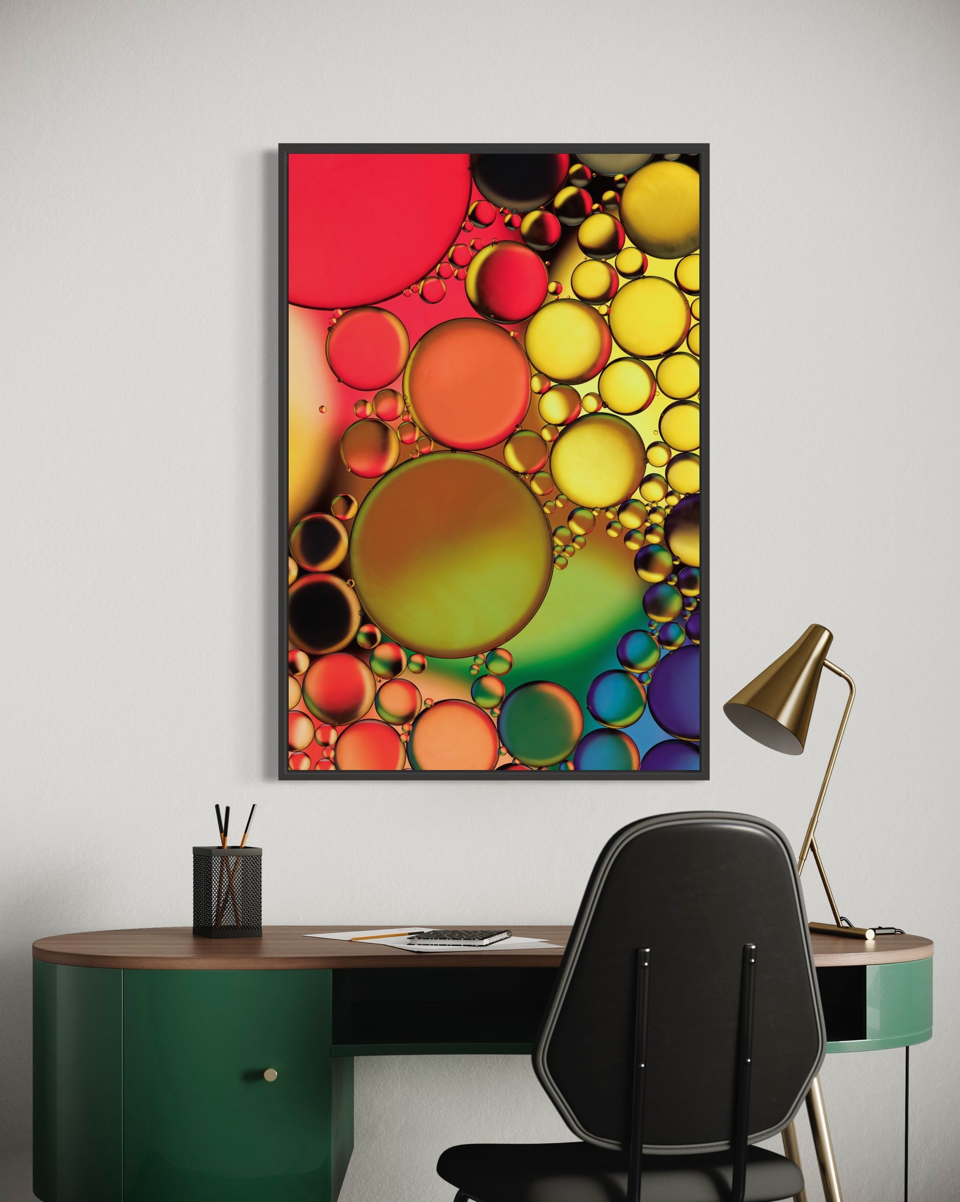 Abstract photograph titled "Jewels" featuring an interplay of oil and water in vibrant orange, yellow, green, blue, and purple hues, printed on high-grade photo paper and mounted under acrylic for depth and clarity. The predominant elements of this image are circular forms and vibrant hues.  The image shows the print hanging over a green desk. 
